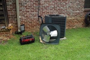 Air Conditioner compressor condenser coil with fan and tools being worked on next to a brick house for repair maintenance.